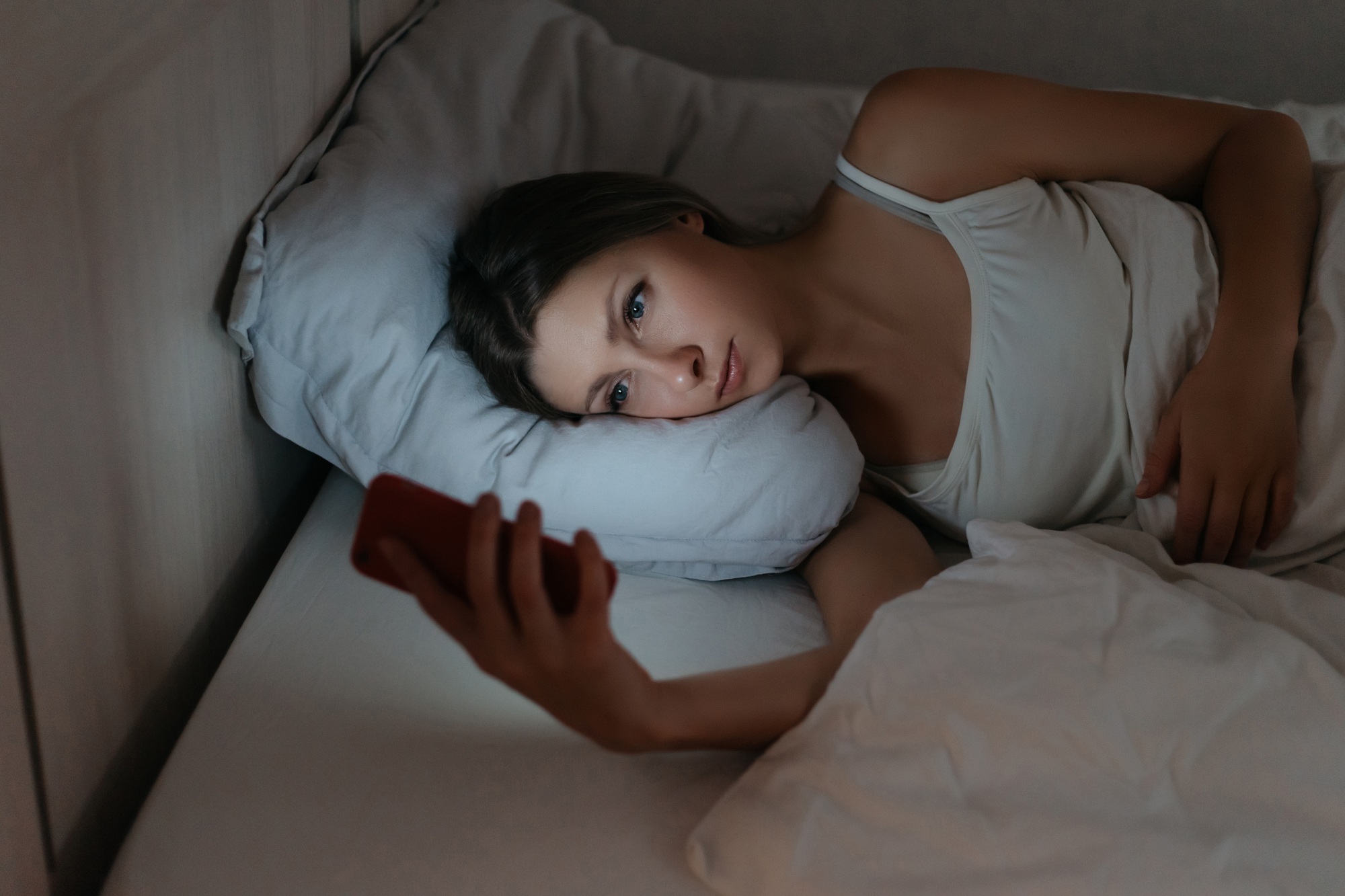 Female using her smartphone in bed at night instead sleeping.