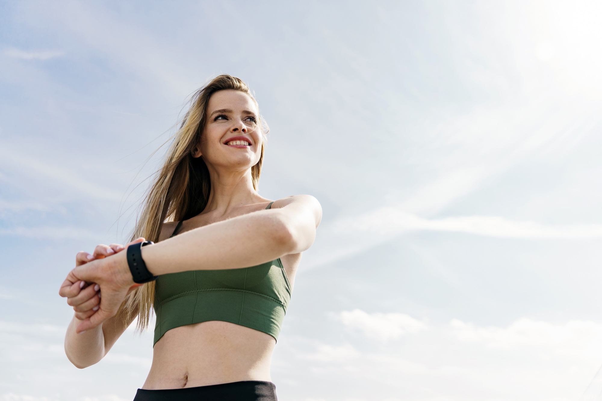 strong woman uses a fitness watch for sports training. The athlete smiles portrait against the sky.